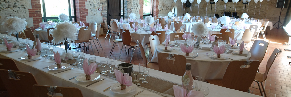 Salle avec tables, chaises, vaisselle, verres, serviettes, fleurs, ballons, fenêtres.