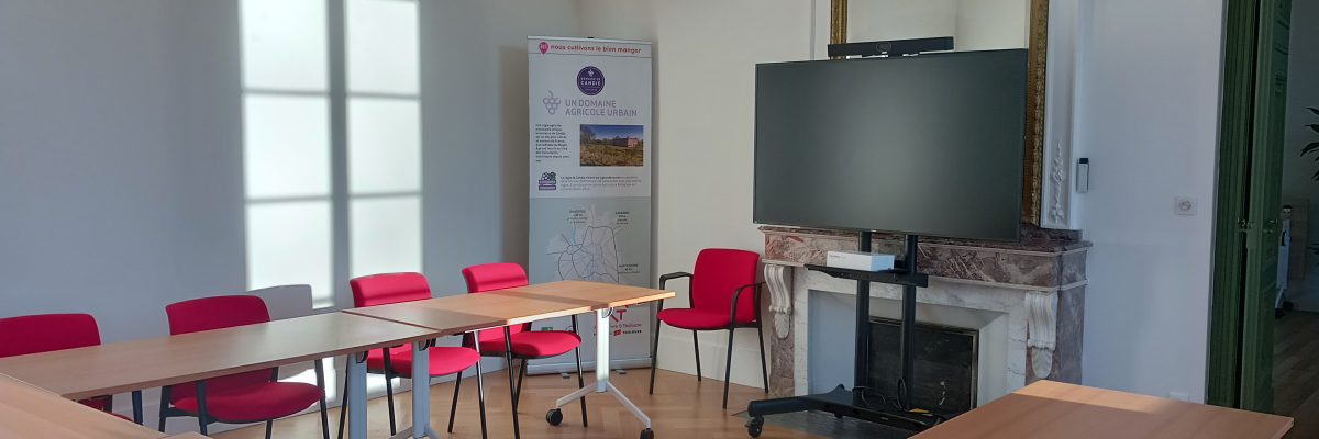 Salle de réunion avec tables, chaises, téléviseur, climatiseur et miroir.