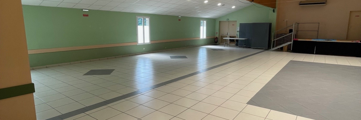 Grande salle avec sol carrelé, miroirs, éclairages suspendus et mur vert.