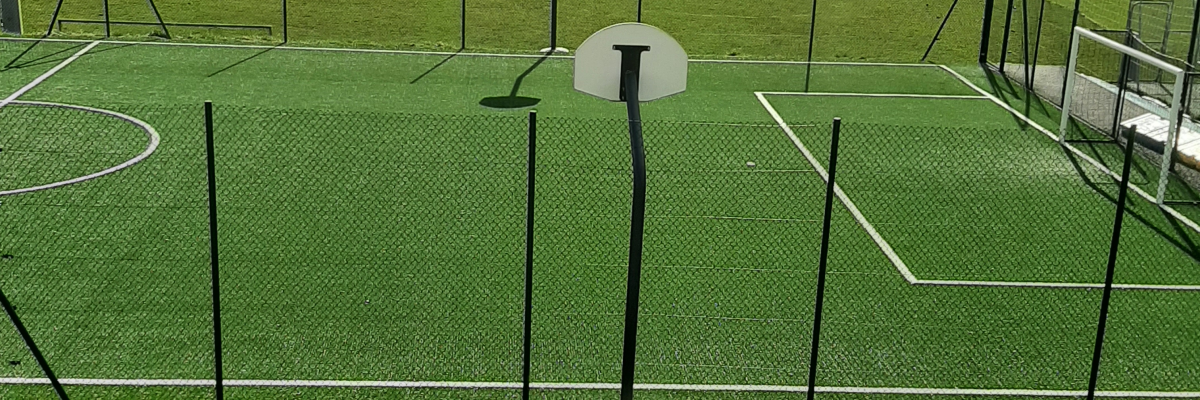 Terrain de foot à 5 avec buts, filets, poteaux et arbres en arrière-plan.