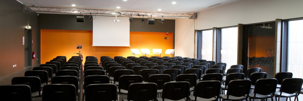 Salle de conférence avec chaises, écran, projecteur et éclairage.
