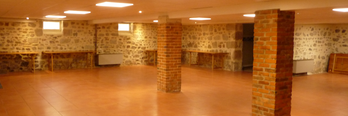 Salle avec murs de pierre, colonnes de brique, sol carrelé, éclairage au plafond.