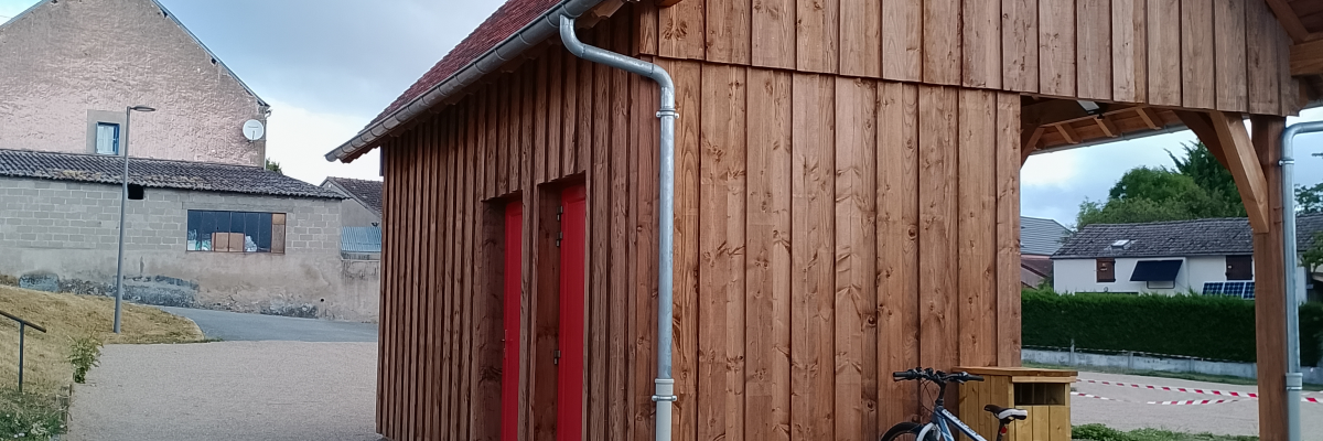 Bâtiment en bois avec porte rouge, vélo jaune, maison en arrière-plan.