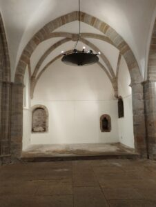 Salle avec voûte, lustre, deux cadres et plateforme.