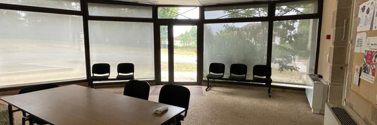 Salle avec table, chaises, luminaire, fenêtre, radiateur, tableau d'affichage.
