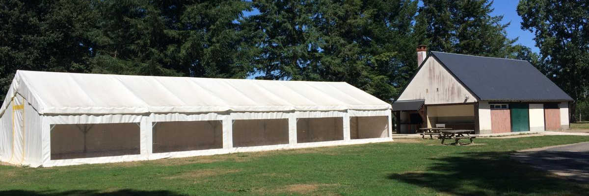 Tente de réception blanche près d'un bâtiment en bois, avec des arbres en arrière-plan.