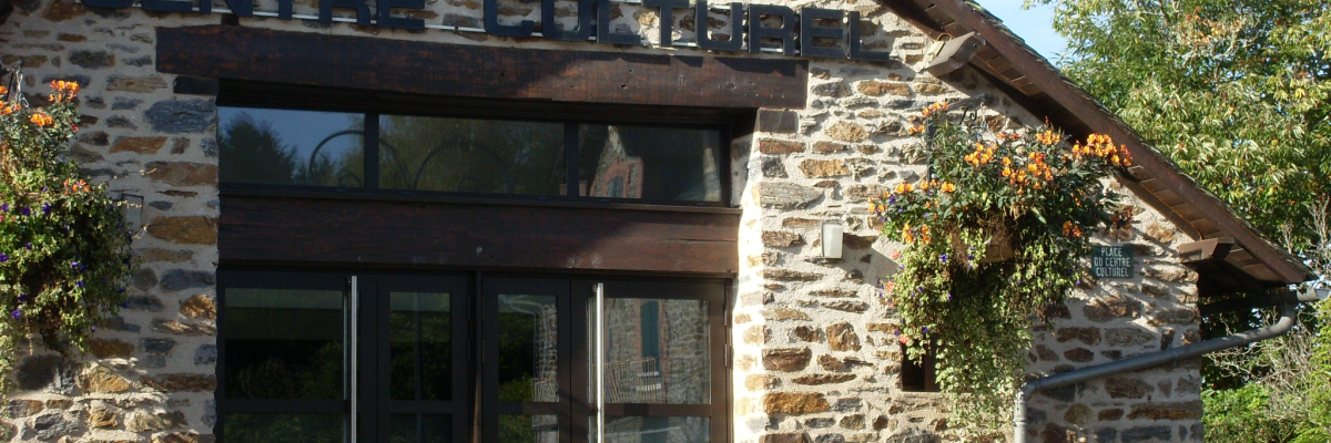Bâtiment en pierre avec entrée vitrée, enseigne "Centre Culturel" et fleurs suspendues.