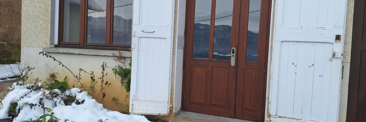 Maison avec porte en bois et fenêtres, neige au sol.