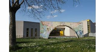 Bâtiment avec arcade, graffitis et escaliers extérieurs, devant un arbre et un champ de fleurs.