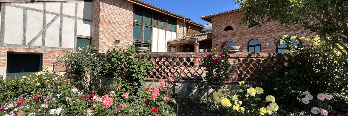 Bâtiment en briques avec un jardin fleuri devant, comprenant une variété de fleurs et de verdure.