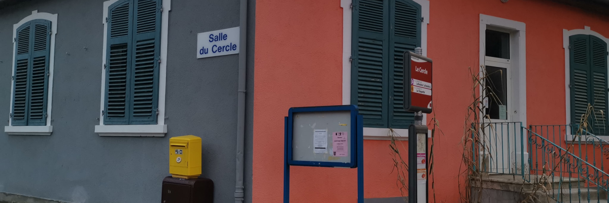 Bâtiment avec façade orange et grise, volets verts, panneaux d'affichage, boîte aux lettres jaune.