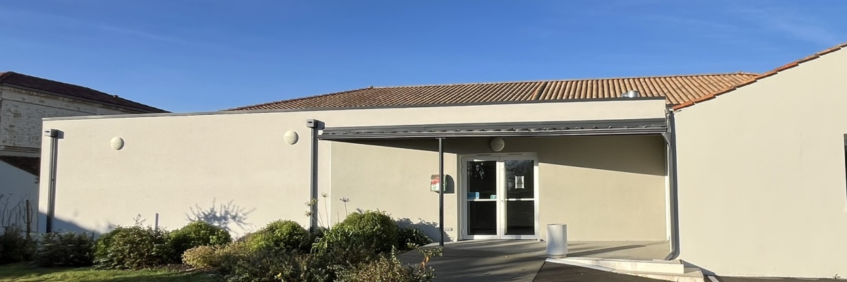 Bâtiment avec entrée principale, porte vitrée, allée et pelouse.