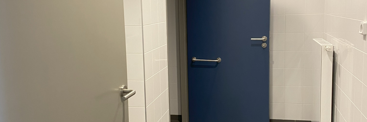 Couloir avec portes, sol carrelé, mur en carreaux et plafonnier.