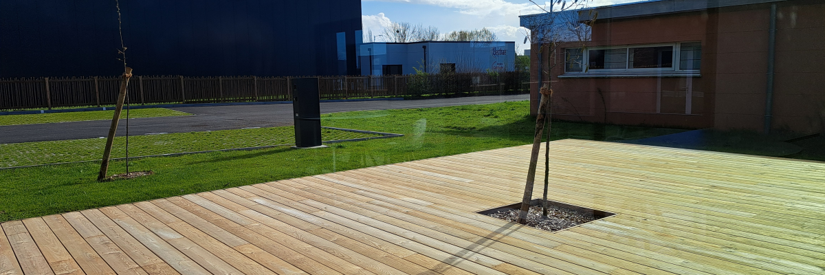 Terrasse en bois avec arbre, bâtiments en arrière-plan.