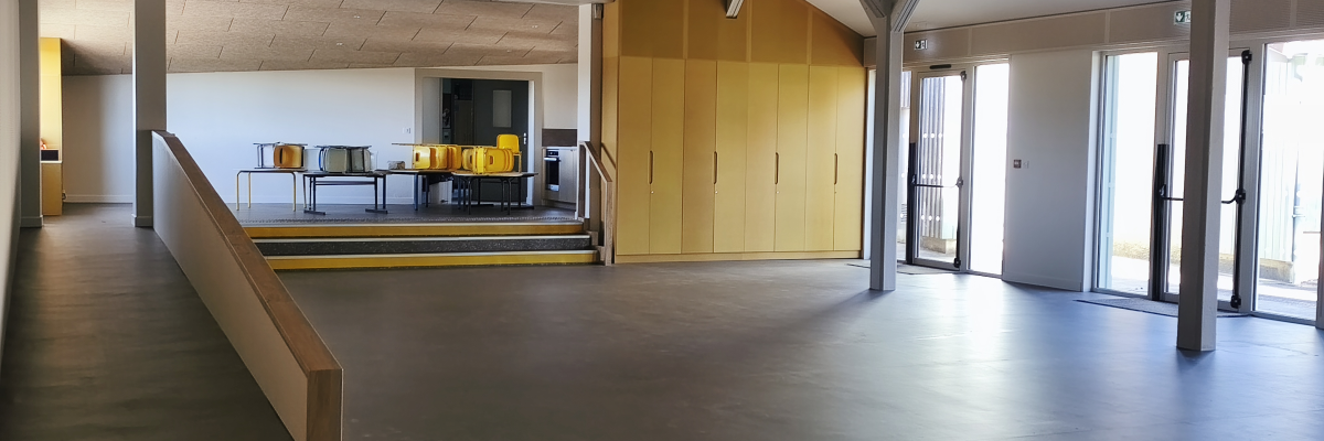 Salle spacieuse avec rampes, mobilier, portes vitrées et grandes fenêtres.