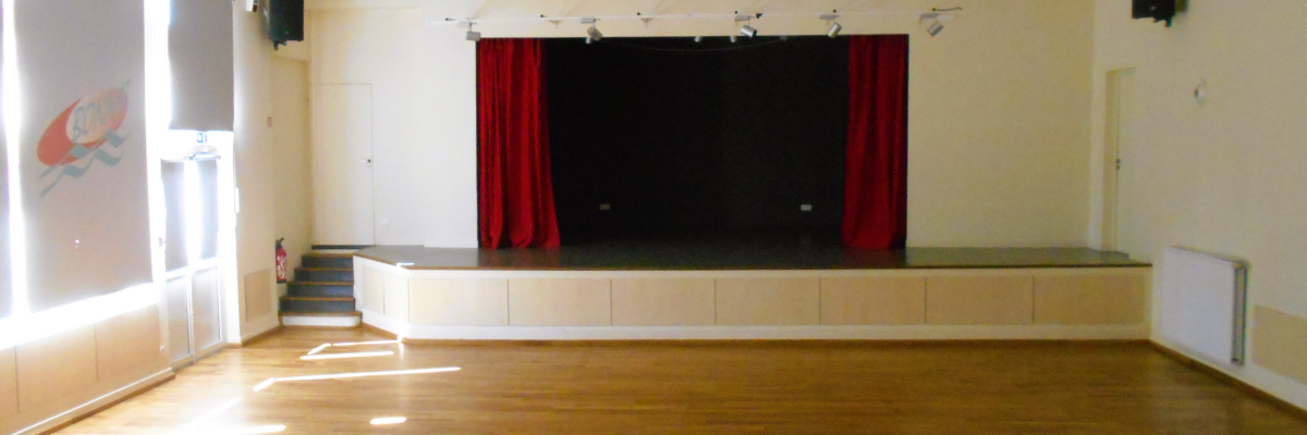 Salle avec scène, rideaux rouges, projecteurs, écran et parquet.