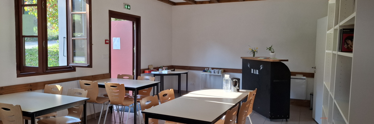 Salle avec tables, chaises, bibliothèques, frigo, évier et fenêtre.