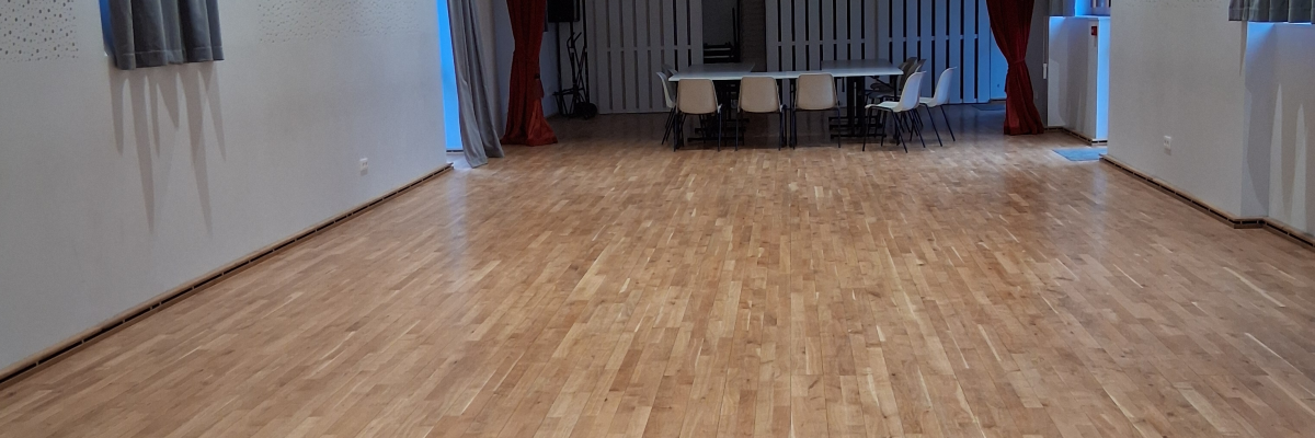 Salle vide avec parquet, tables, chaises et rideaux.