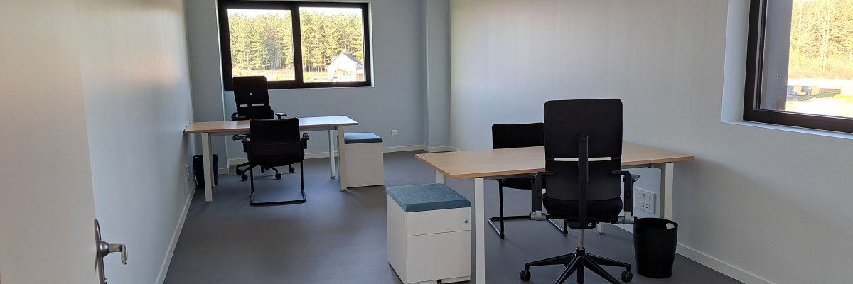 Bureau avec quatre chaises, deux tables, deux ordinateurs et deux fenêtres.