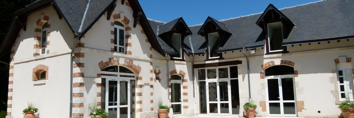 Bâtiment à deux étages avec pignons, briques apparentes, portes vitrées et pots de fleurs.