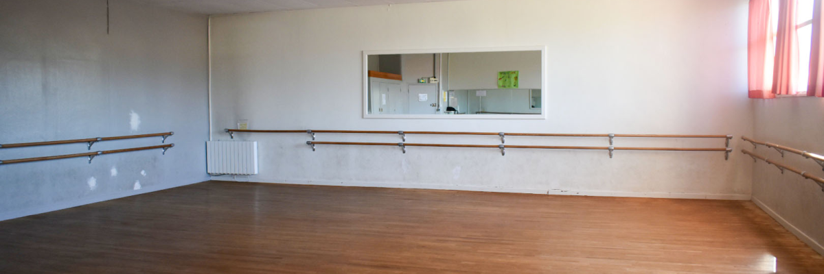 Salle avec barres murales, miroirs, sol en bois et éclairage suspendu.