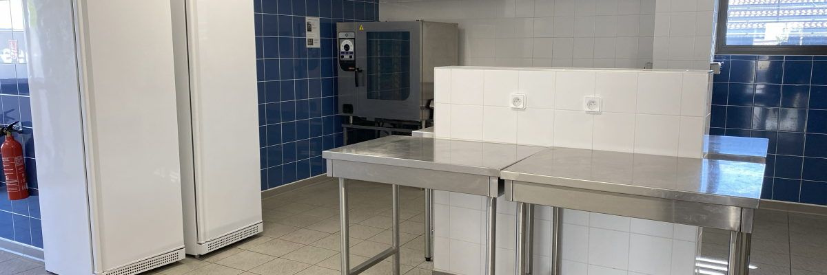 Cuisine avec réfrigérateurs, plans de travail, hottes et carrelage bleu.