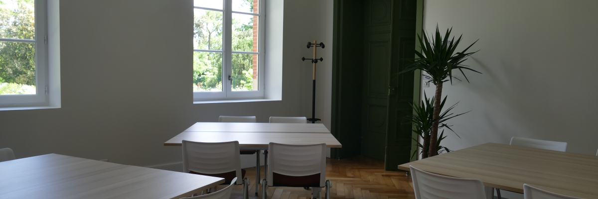 Salle avec tables, chaises, porte, fenêtre, plante et extincteur.