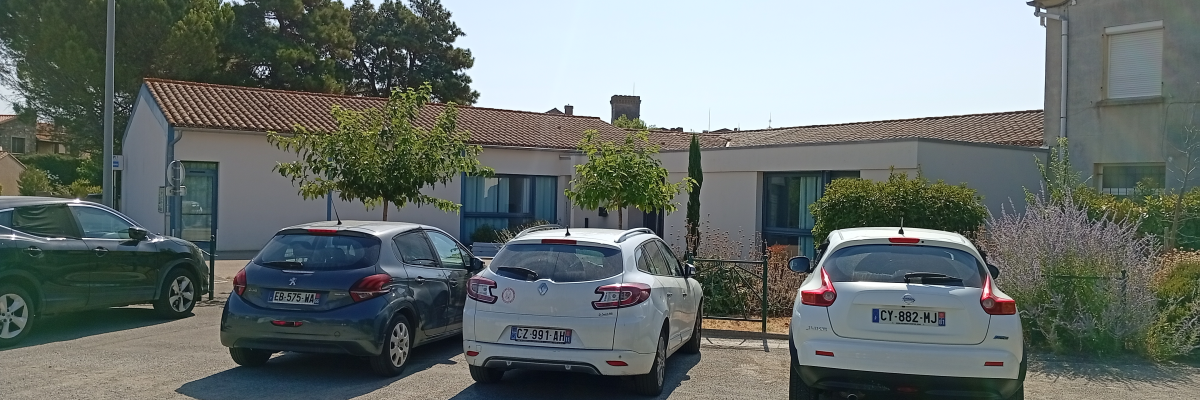 Parking avec trois voitures, lampadaire et maison en arrière-plan.
