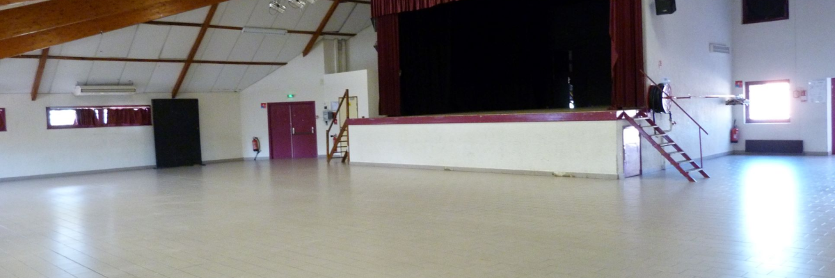 Salle avec scène, rideau, gradins, portes et projecteurs.