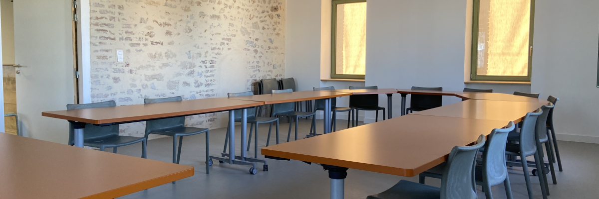 Salle de classe avec tables, chaises, tableau blanc et fenêtres.