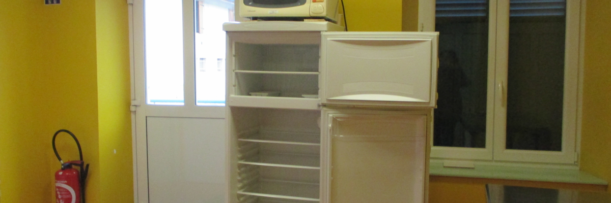 Cuisine avec réfrigérateur, micro-ondes, étagères et extincteur.