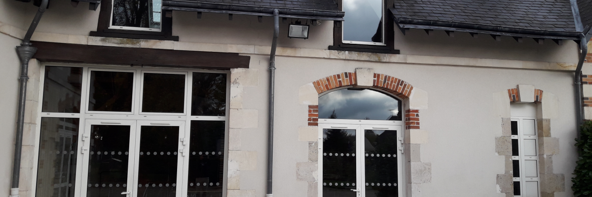 Maison avec toits pentus, fenêtres et portes en verre, briques apparentes, cheminée et pavage extérieur.