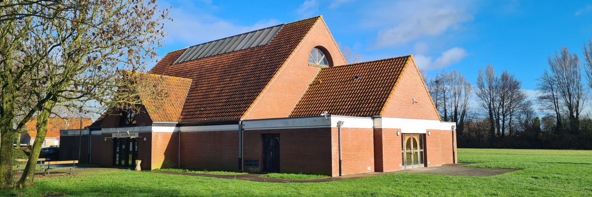Bâtiment en briques avec toit en tuiles, pelouse et arbres.