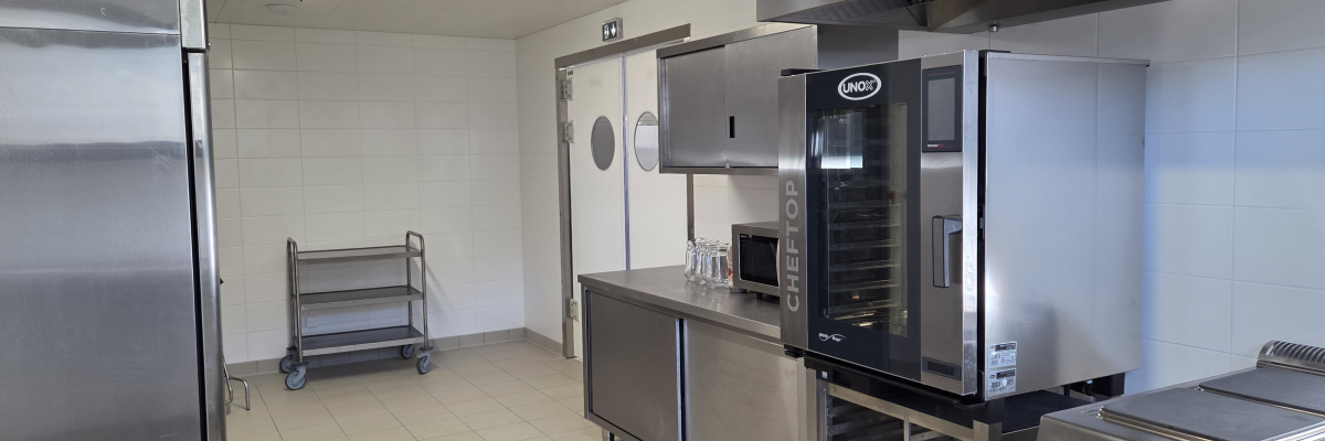 Cuisine professionnelle avec plans de travail, fours, micro-ondes, chariot et plaques de cuisson.