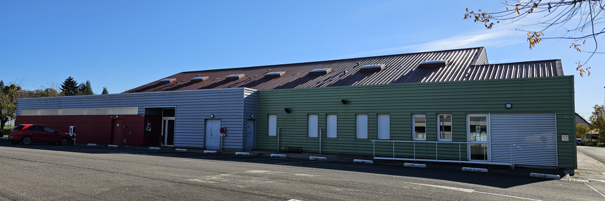 Bâtiment avec murs verts et blancs, toit métallique, voitures, arbre et parking.
