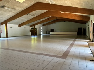 Salle vide avec sol carrelé, poutres en bois, portes et fenêtres.