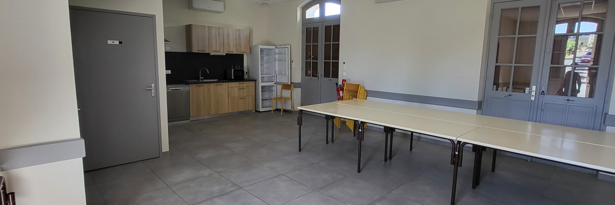 Pièce avec table, chaises, cuisine et portes.