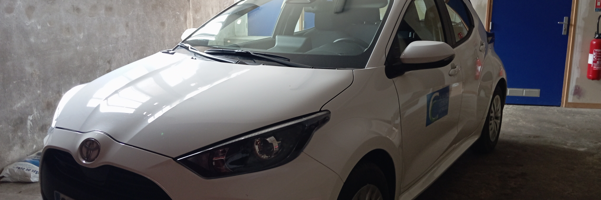 Voiture blanche garée dans un garage avec portes bleues et extincteurs.