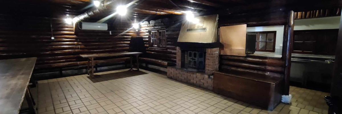 Pièce en bois avec cheminée, bancs, table et lumières.