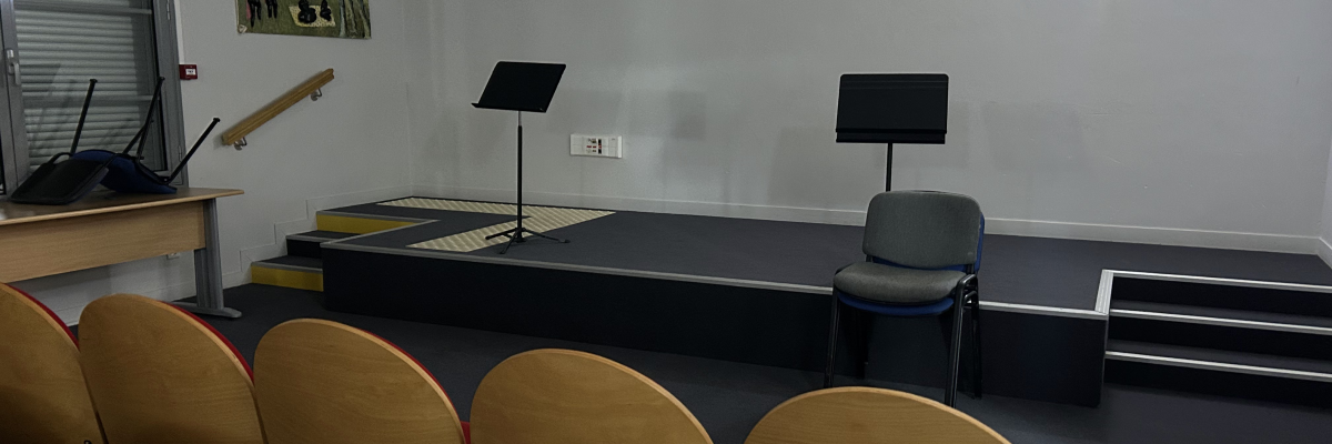 Salle avec pupitre, tableau, pied de micro, sièges alignés et tableau d'affichage.