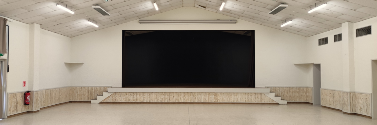 Salle avec grand écran, sol lisse, murs blancs, plafond voûté, lumières et ventilateurs suspendus, pas de meubles visibles.
