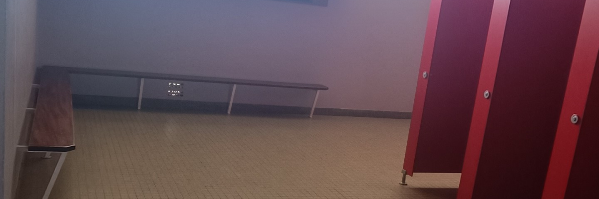 Salle avec bancs, cabines rouges et sol carrelé.