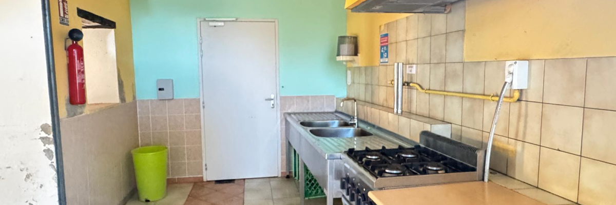 Cuisine avec plaques de cuisson, évier, hotte, table de travail, poubelle verte et extincteur.