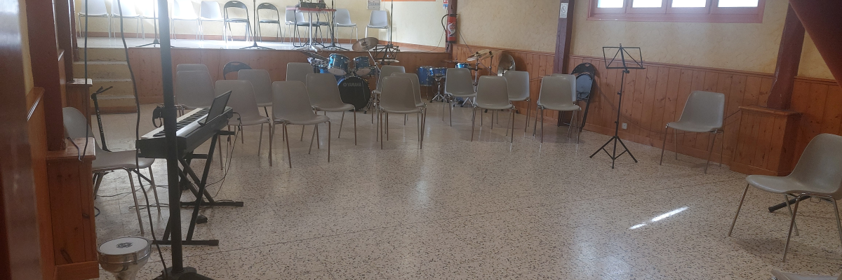 Salle de répétition avec chaises, pupitres, piano électrique, amplificateur et micro sur pieds.