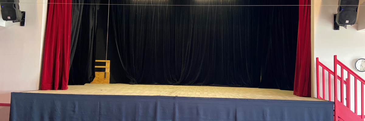 "Scène de théâtre avec rideaux noirs et rouges, projecteurs, et barrière rouge."