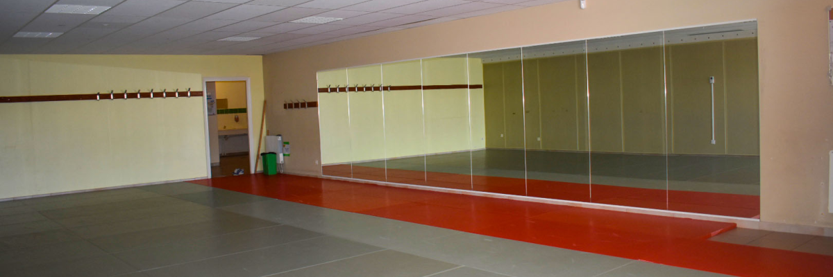 Salle vide avec miroirs, sol carrelé, porte et poubelle verte.