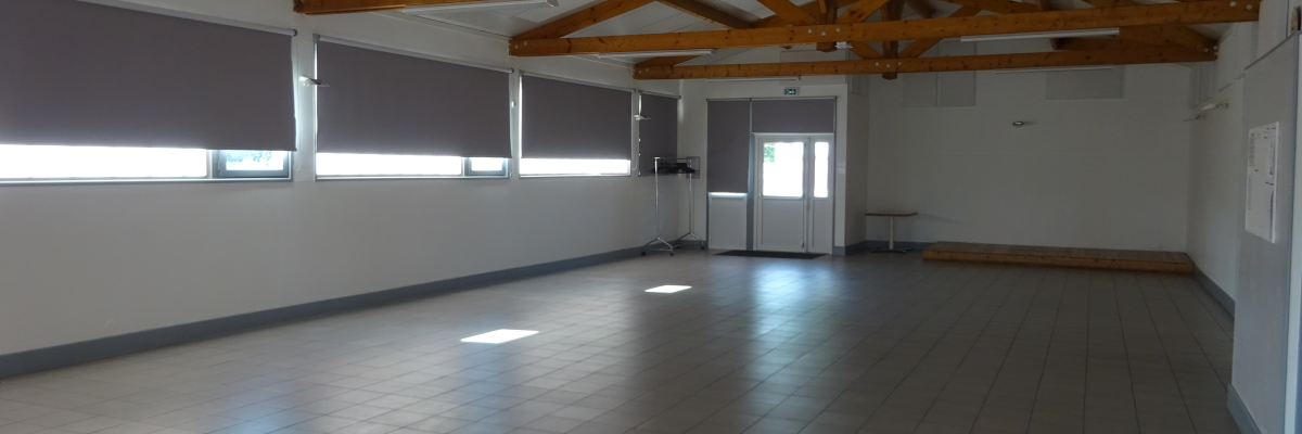 Salle vide, plancher carrelé, poutres en bois, fenêtres avec stores, porte.