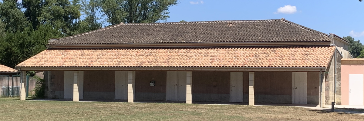Bâtiment avec toit en tuiles, colonnes et portes ouvertes. Pelouse devant.