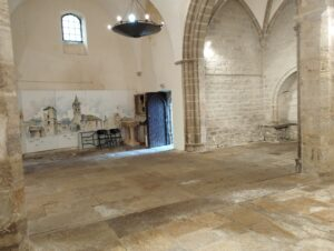 Salle avec sol en pierre, meubles anciens, porte en bois et lustre suspendu.