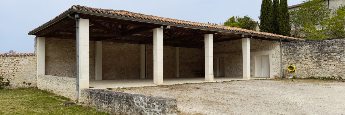 Abri en pierre avec toit, colonnes et porte blanche, entouré d'arbres et de murs.